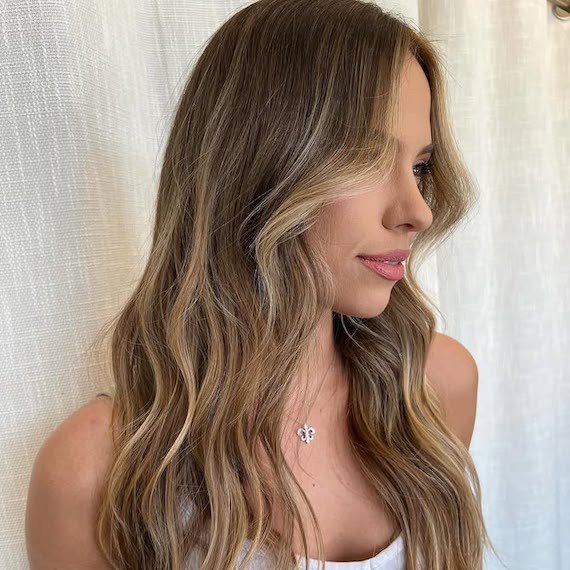 Side profile of model with dark blonde, wavy hair featuring beachy balayage.