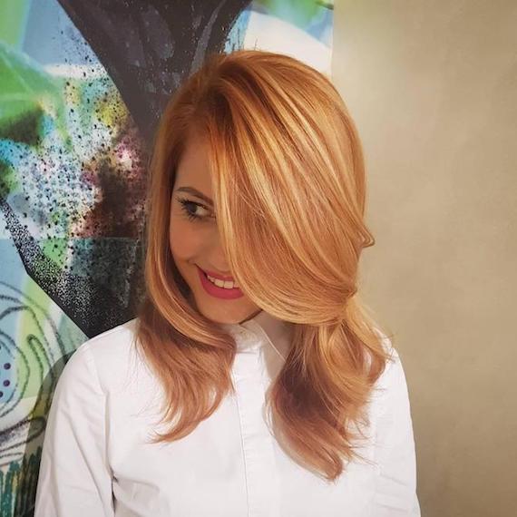 Woman wearing white shirt and showing off strawberry blonde highlights, created using Wella Professionals. 