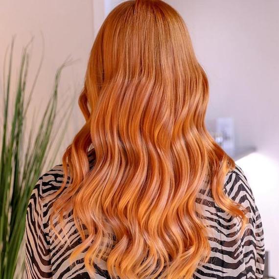 Back of a woman’s head showing long, wavy, strawberry blonde ombre hair, created using Wella Professionals. 