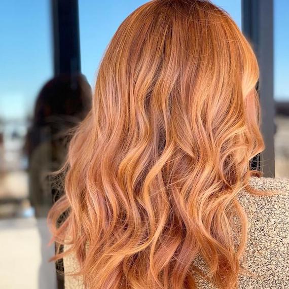 Back of a woman’s head showing long, wavy, strawberry blonde balayage, created using Wella Professionals. 