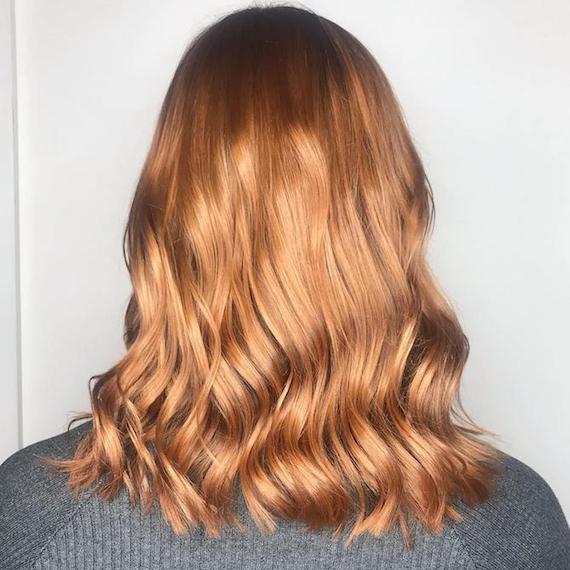 Back of a woman’s head showing mid-length, wavy, strawberry blonde balayage, created using Wella Professionals. 