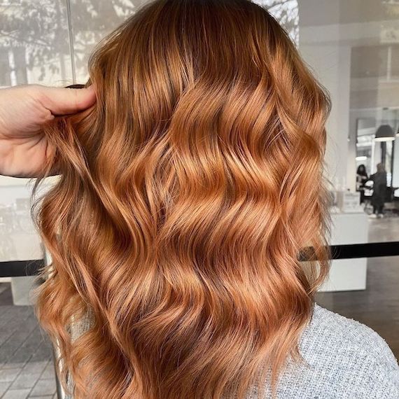 Back of model’s head showing long, wavy hair with a dark root shadow and strawberry blonde balayage.