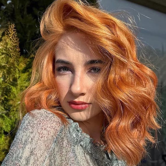 Model with wavy, shoulder-length, copper-tinted strawberry blonde hair.