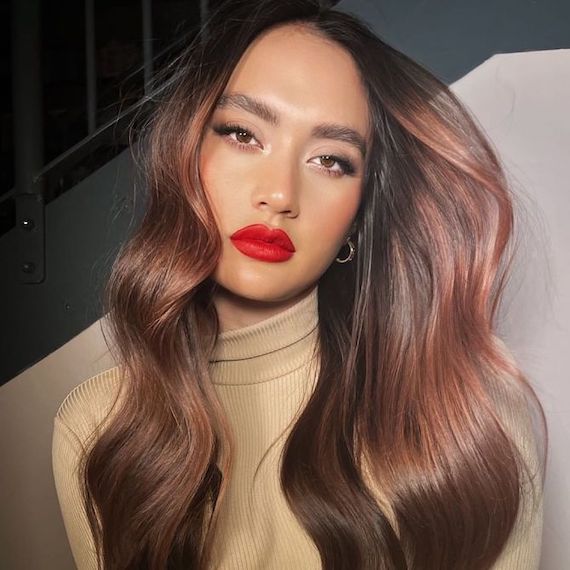 Model with brown hair and subtle strawberry balayage faces the camera.