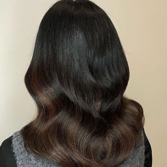 Back of woman’s head with long, black hair, retouched roots and toffee balayage, created using Wella Professionals. 