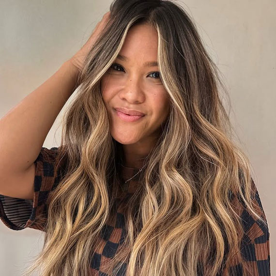 Model with long, wavy, hair featuring a dark brown root stretch and beachy blonde balayage.