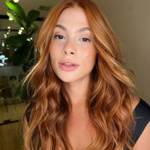 Model with warm, peachy, copper-colored hair styled in tousled waves.