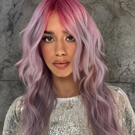 Model with long, wavy hair that’s bright pink at the roots and lilac through the lengths.