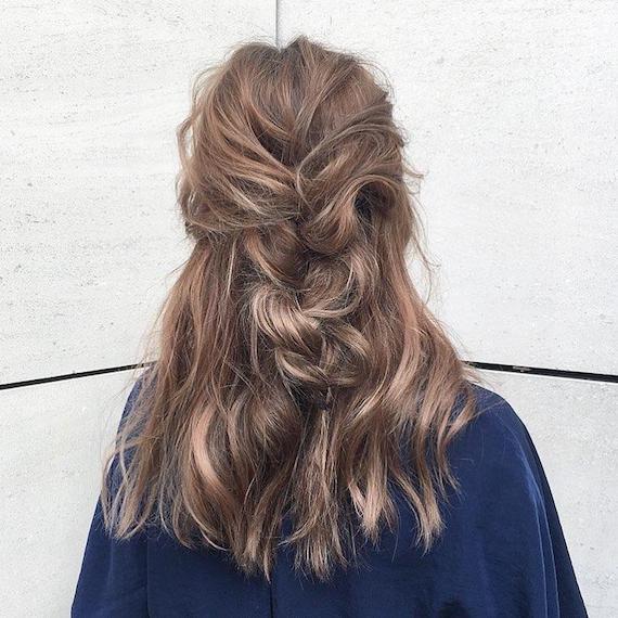 Photo of the back of a woman’s head with tousled brunette hair and blonde highlights, tied into a loose plait. Look created by Wella Professionals.