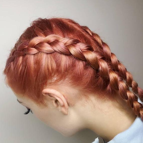 Close-up image of side of woman’s head, wearing pink hair color and boxer braids, created by Wella Professionals.