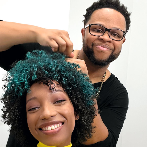 : Model with short, black, curly hair featuring a bold teal color block section.