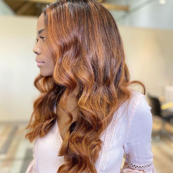 Model with long, dark, loosely curled hair, featuring sun-kissed, strawberry blonde highlights. 