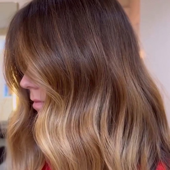 Side profile of model with long, toffee bronde hair featuring highlights through lengths and ends.