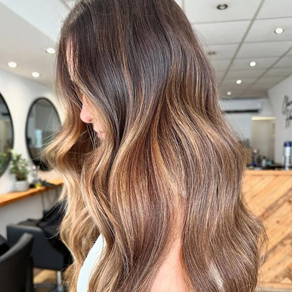 Model with long, brown, wavy hair featuring sun-kissed bronde highlights through lengths and ends.