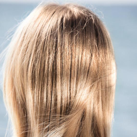 Back of model’s head with beachy blonde hair blowing in the breeze.