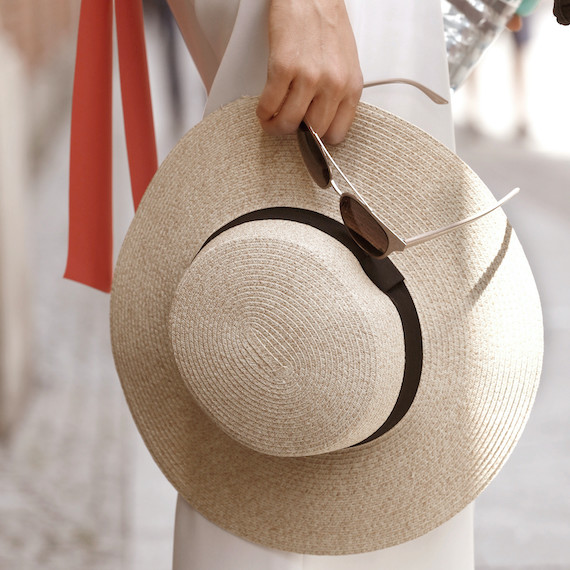 Model holds sun hat and sunglasses down by their side.