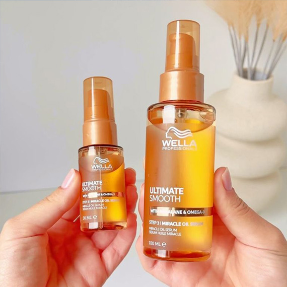 Model holds up mini and full-size bottles of ULTIMATE SMOOTH Miracle Oil Serum.
