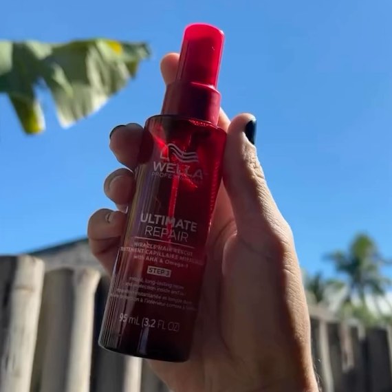 A bottle of ULTIMATE REPAIR Miracle Hair Rescue is held up in front of blue sky.