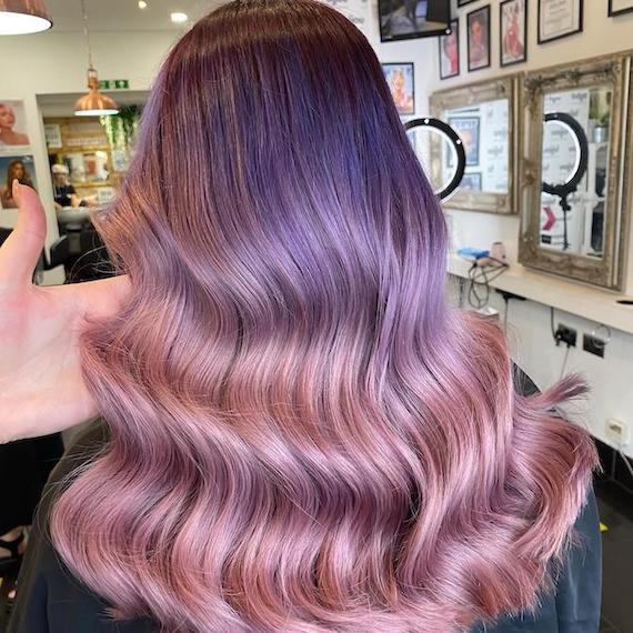 Back of model’s head with long, glossy hair featuring deep purple tones melting into pastel pink. 