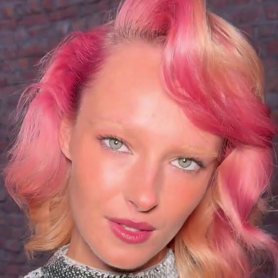 Model with shoulder-length hair featuring pink and peach sunset tones.