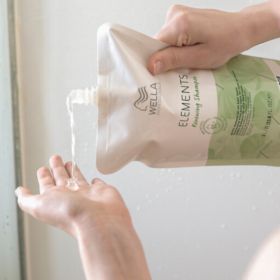 A model squeezes Elements Renewing Shampoo into the palm of their hand from a refill pouch.