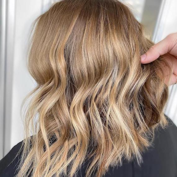 Back of woman’s head with warm blonde, wavy hair and golden blonde teasy lights, created using Wella Professionals.