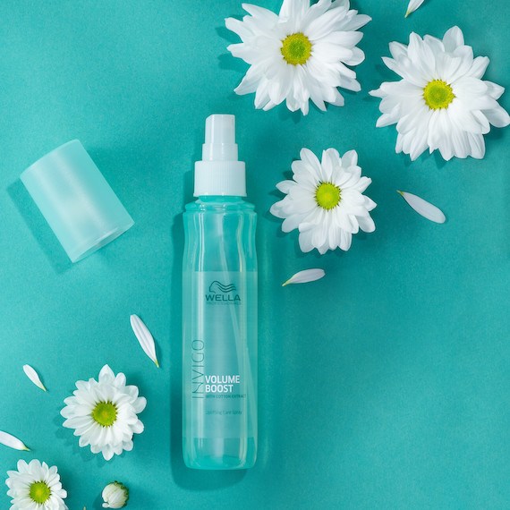 INVIGO Volume Boost Leave-In Spray on a green surface surrounded by flowers.