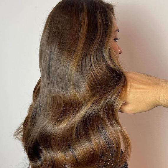 Back of woman’s head with long, wavy, chocolate brown hair and toffee highlights.