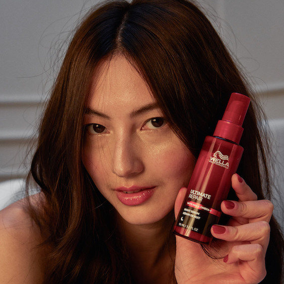 Model with dark brown hair in a dimmed room holds up ULTIMATE REPAIR Night Serum.