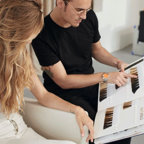 Woman and hairdresser look through a book of Koleston Perfect hair color swatches.