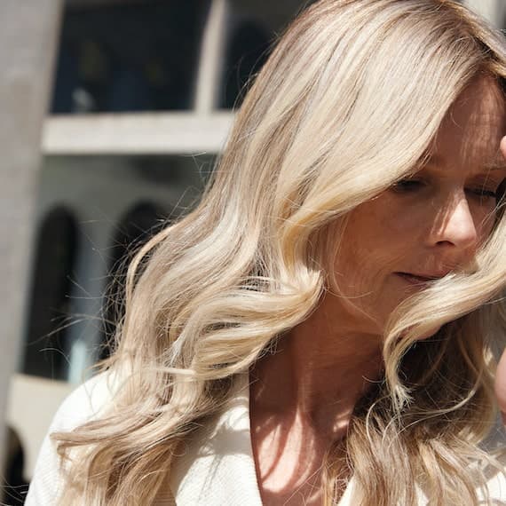 Close-up of woman as her blonde, wavy hair is swept by the breeze.