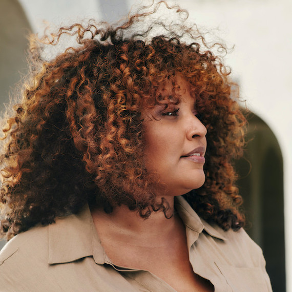 Woman with curly, brunette hair and chestnut highlights gazes off to the side.