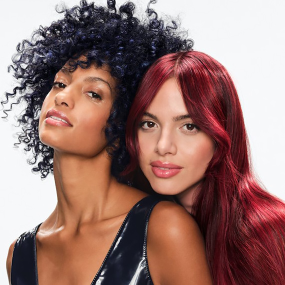 Two models stand together – one with blue, curly hair and one with long, straight, cherry red hair.