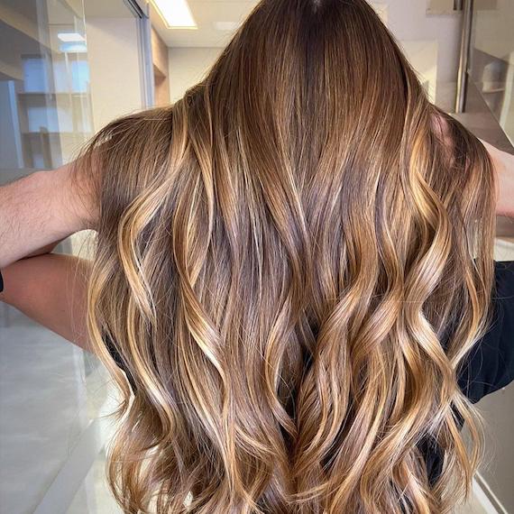 A person faces away from the camera showing their long wavy walnut blonde hair colour with buttercream highlights