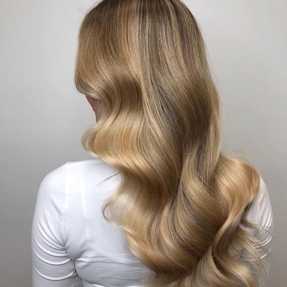 Photo showing the back of a woman’s head with long, loosely-curled, dark blonde hair. Created using Wella Professionals. 