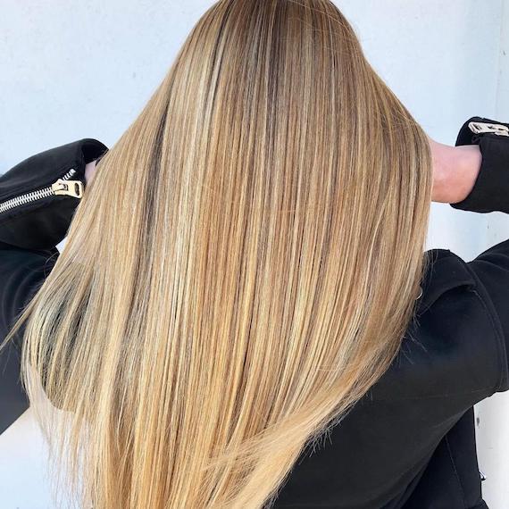 Das Foto zeigt die Rückseite des Kopfes einer Frau mit langen, superglatten, goldblonden Haaren. Kreiert mit Wella Professionals.