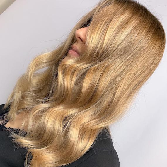 Side profile of a woman with long, wavy, honey blonde hair. Created using Wella Professionals. 