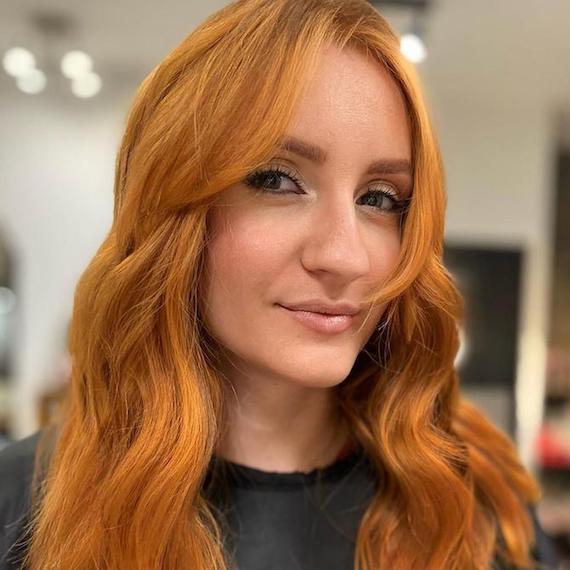 Headshot of a person with brown eyes and copper blonde hair styled in waves