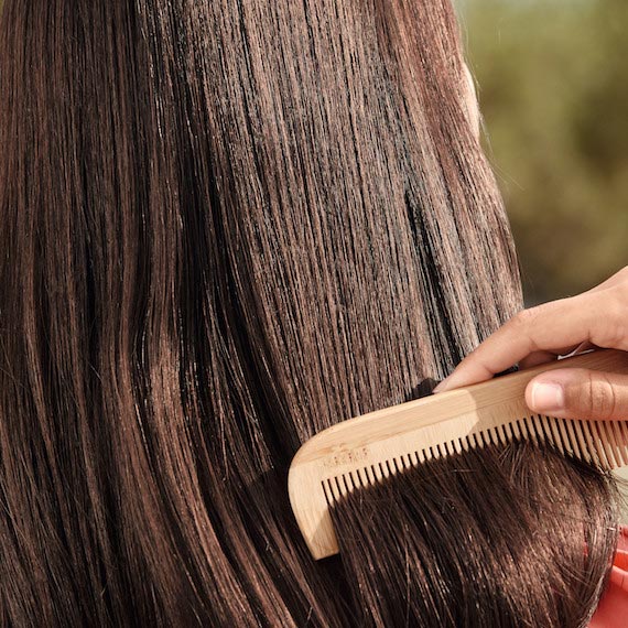 Close up of hand brushing smooth, brown hair with a wooden comb. 