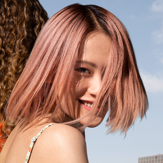 Woman with pastel pink bob haircut smiles at camera.