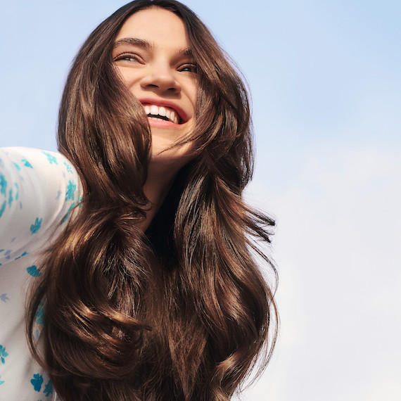 Woman with long, wavy, brunette hair smiles as she gazes into the distance.