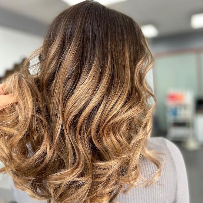 Back of woman’s head with loosely curled hair and caramel balayage.