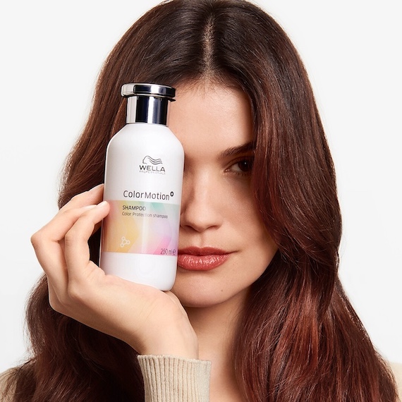 A model with dark brown hair holds ColorMotion+ Color Protection Shampoo in front of face.