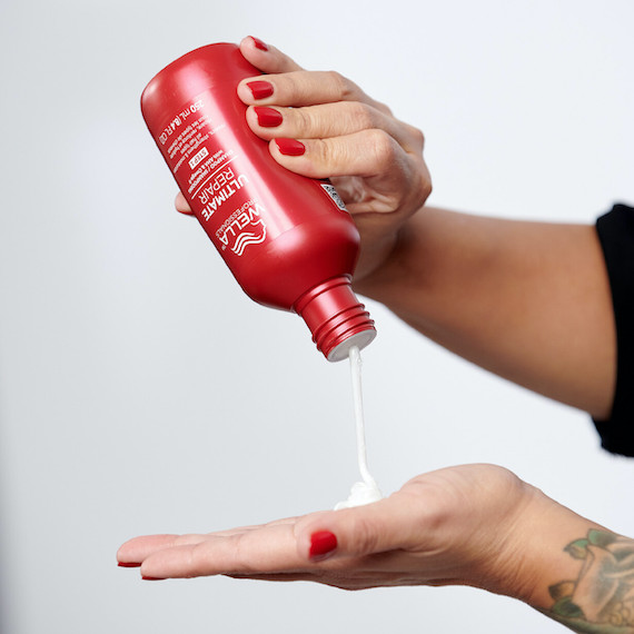 Model holds a bottle of Ultimate Repair Shampoo and pours product into the palm of their hand.