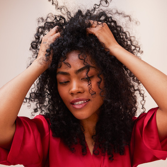 A model runs their hands through their long, dark, curly hair. 