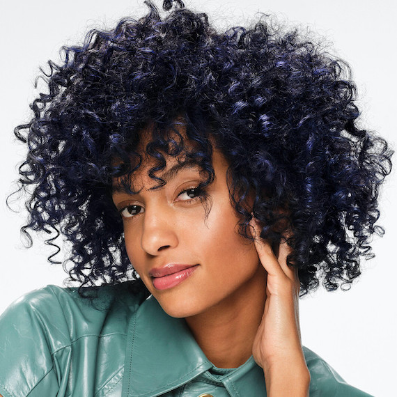 Model with short, dark, curly hair, featuring navy blue melted highlights.