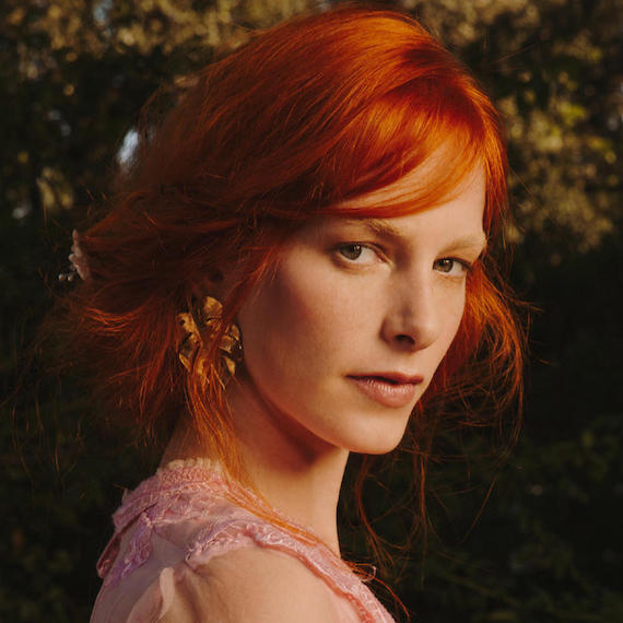 Model with red hair styled by Wella Professionals into a low, loose bun looks over her shoulder