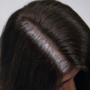 Top of woman’s head with brunette hair and stubborn gray roots. 