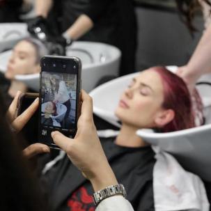 Hairdresser using a phone to take a photo of a woman having her hair washed.  