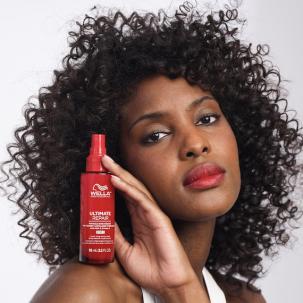 Model mit lockigem dunklem Haar hält eine rote Flasche von Wella Professionals Ultimate Repair Miracle Hair Rescue auf der Schulter.